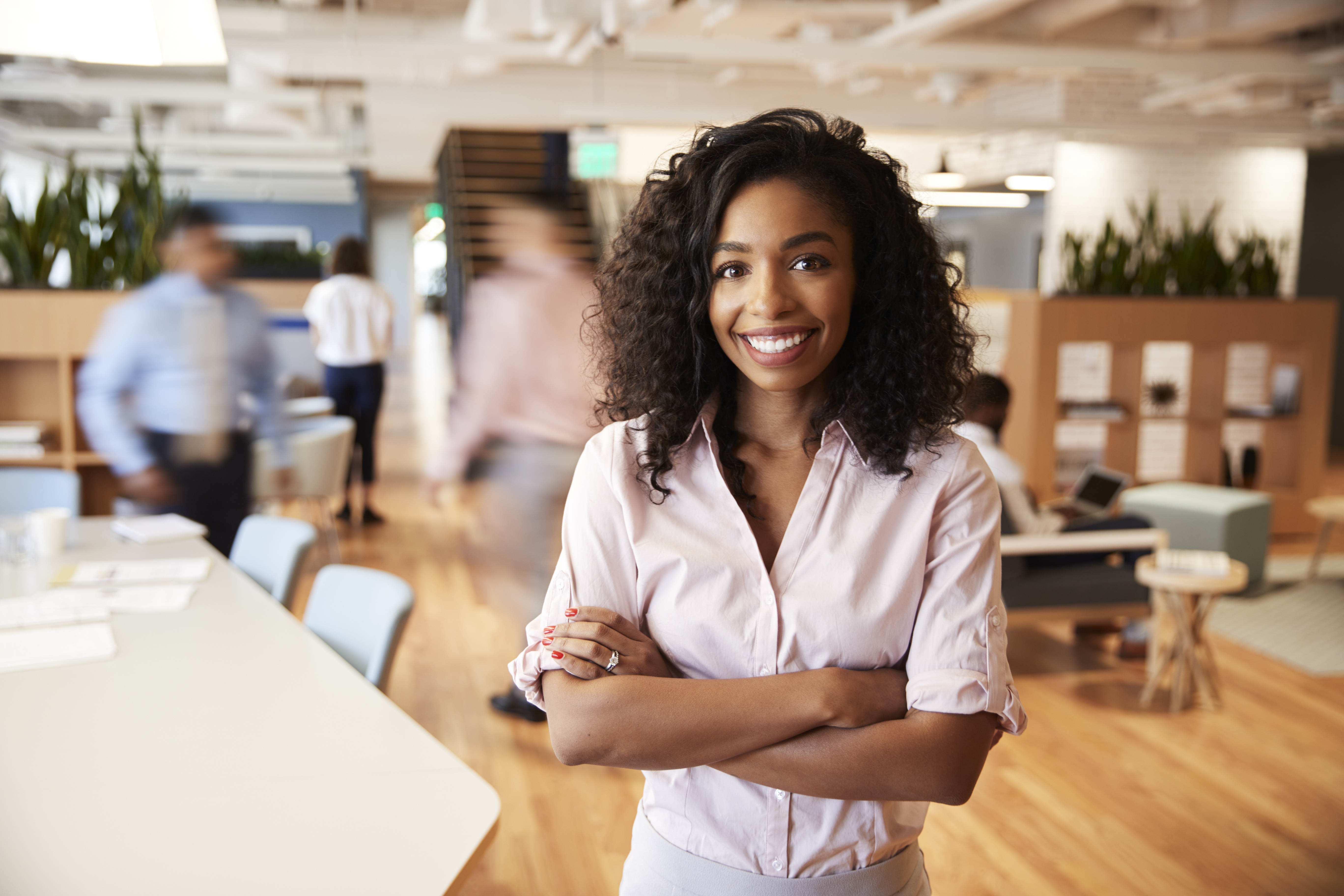 Portrait Of Businesswoman In Busy Modern Office With Blurred Colleagues Working In Background